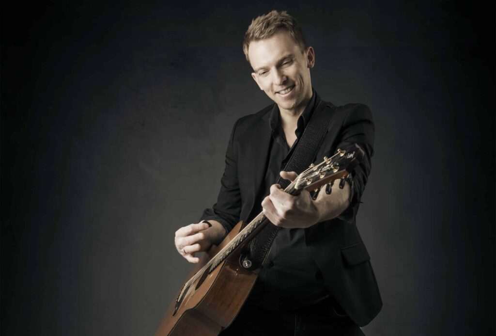 Søren Okholm med guitar, mørkt portræt
