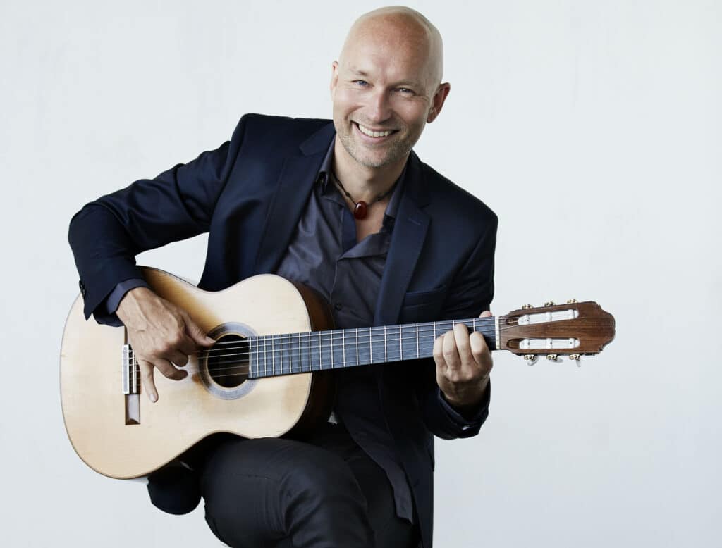 Mand spiller klassisk guitar siddende i et lyst rum