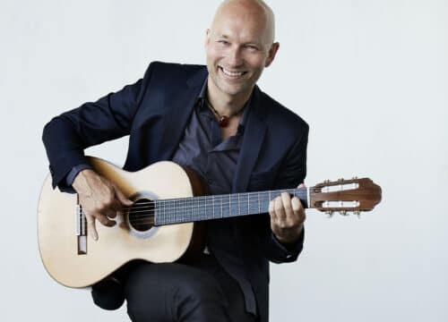 Mand spiller klassisk guitar siddende i et lyst rum