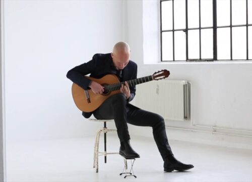 Guitarist spiller klassisk guitar ved et vindue