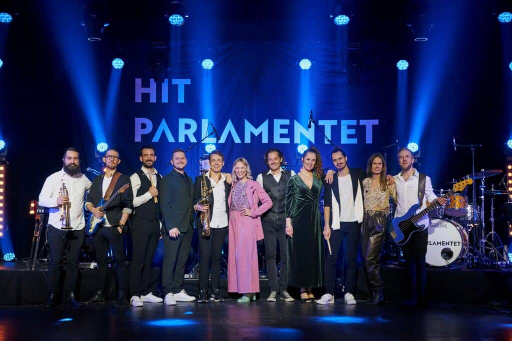 Hit Parlamentet på scenen foran navne-banner i blåt lys